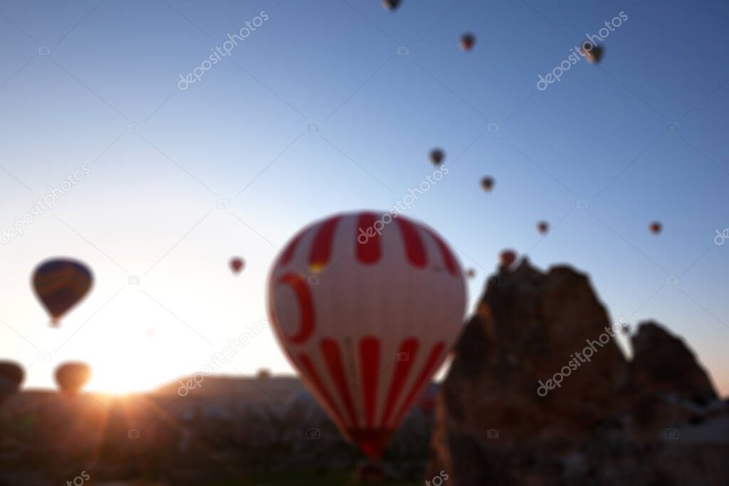 Blurred view on hot air balloons with Turkish symbolic on blue clear sunlight sky and fairy chimneys rock formations at sunrise. Use as background