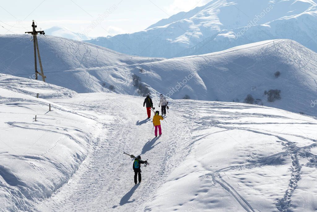 Skiers and snowboarders on snow road at sun winter morning. Caucasus Mountains, Georgia, region Gudauri.