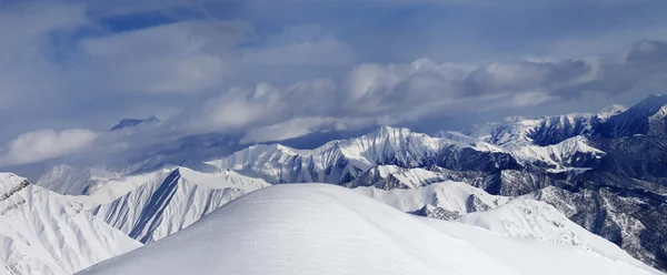 Fuera de pista cuesta cubierto de nieve y las montañas nubladas —  Fotos de Stock