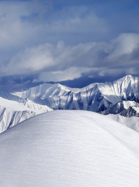 Top of off piste snowy slope and cloudy mountains clipart