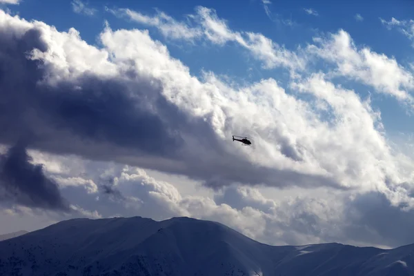 Helicopter in cloudy sky and winter mountains — Stock Photo, Image