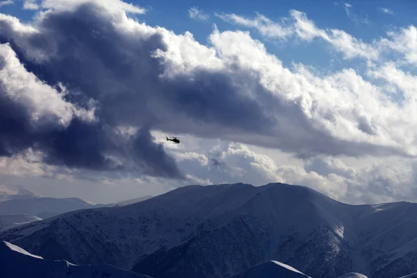 Helicopter in cloudy sky and winter mountains in evening — Stock Photo, Image