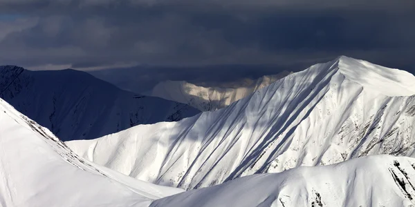 Panoramautsikt över snötäckta solbelysta bergen och mulen himmel — Stockfoto