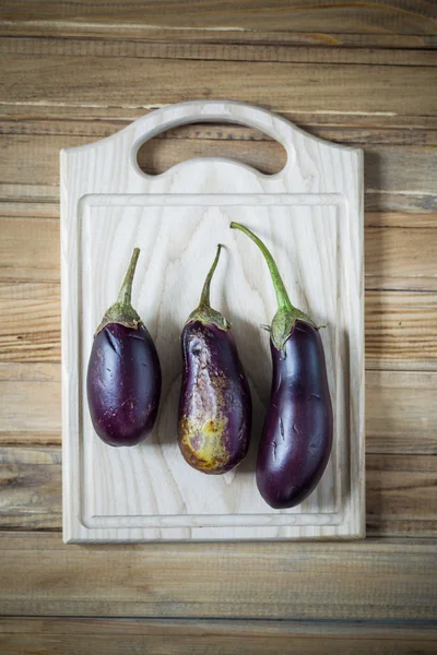 Tres berenjenas maduras en una tabla de cortar — Foto de Stock