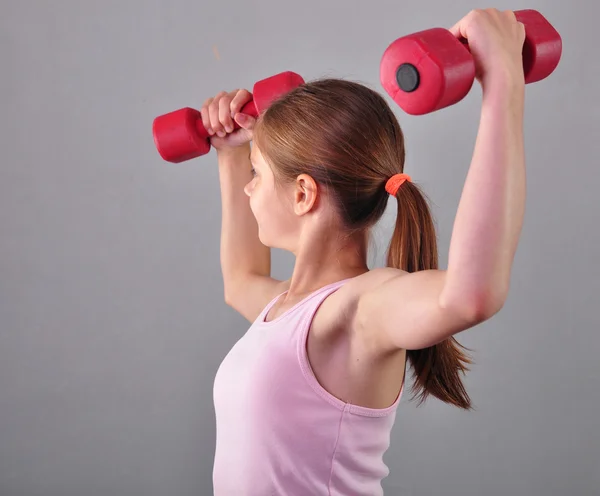 Adolescente chica deportiva está haciendo ejercicios para desarrollar músculos aislados en el fondo gris. Concepto de estilo de vida saludable deportivo. Deportiva infancia. Adolescente haciendo ejercicio con wieghts . — Foto de Stock