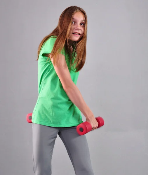 Adolescente menina esportiva está fazendo exercícios para desenvolver músculos em fundo cinza. Esporte conceito de estilo de vida saudável. Infância desportiva. Adolescente exercício com wieghts . — Fotografia de Stock