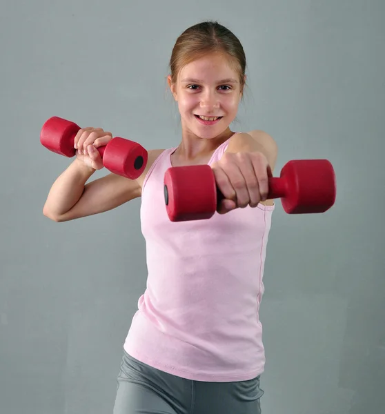 Adolescente chica deportiva está haciendo ejercicios para desarrollar los músculos en el fondo gris. Concepto de estilo de vida saludable deportivo. Deportiva infancia. Adolescente haciendo ejercicio con wieghts . — Foto de Stock