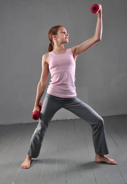 Looking down teenage sportive girl is doing exercises to develop with dumbbells muscles isolated on grey background. Sport healthy lifestyle concept. Sporty childhood. Teenager exercising with weights — Stock Photo, Image