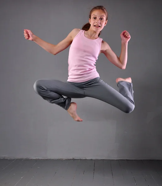 Giovane ragazza muscolosa sana che salta e balla in studio. Bambino che si esercita con il salto su sfondo grigio . — Foto Stock