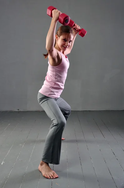 十几岁的女孩与哑铃，研制与哑铃锻炼肌肉在灰色的背景上。充分长的十几岁的孩子锻炼与权重的画像. — 图库照片