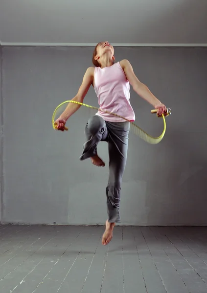 Здоровая молодая мускулистая девочка-подросток прыгает по веревке в студии. Детские упражнения с прыжками на сером фоне . — стоковое фото