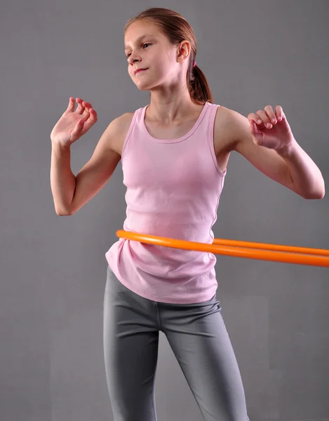 Teenage sportive girl is doing exercises with hula hoop to develop muscle on grey background. Having fun playing game . Sport healthy lifestyle concept. Sporty childhood. Teenager exercising with tool — 图库照片