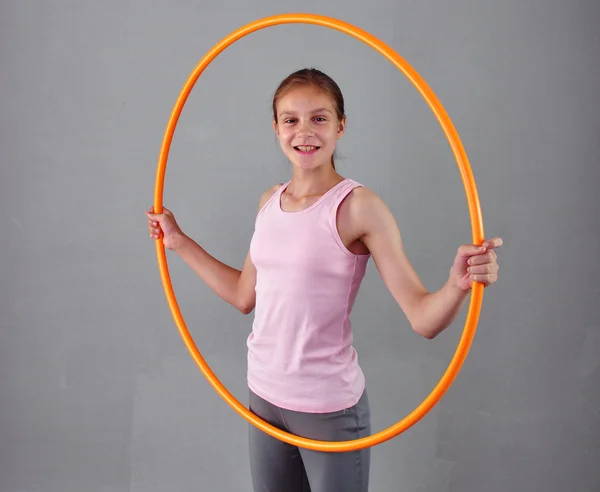 Chica deportiva adolescente está haciendo ejercicios con hula hoop para desarrollar músculo sobre fondo gris. Divirtiéndose jugando. Concepto de estilo de vida saludable deportivo. Deportiva infancia. Adolescente haciendo ejercicio con la herramienta — Foto de Stock