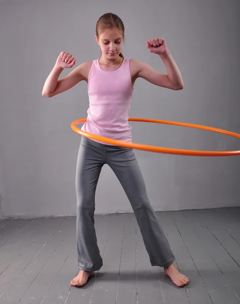 Teenage sportive girl is doing exercises with hula hoop to develop muscle on grey background. Having fun playing game . Sport healthy lifestyle concept. Sporty childhood. Teenager exercising with tool — Stok fotoğraf