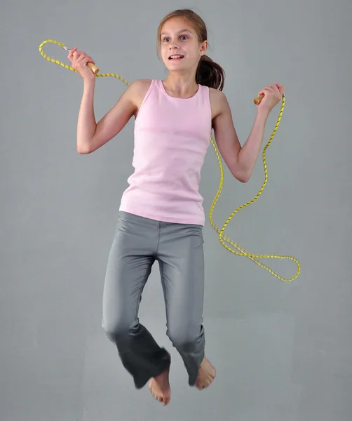 Healthy young muscular teenage girl skipping rope in studio. Child exercising with jumping high on grey background. — Zdjęcie stockowe