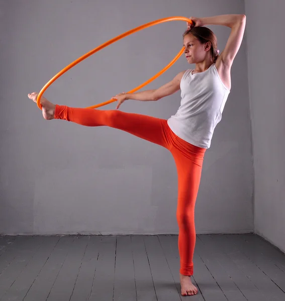 Teenage sportive girl is doing exercises with hula hoop t on grey background. Having fun playing game . Sport healthy lifestyle concept. Sporty childhood. Teenager exercising with tool. — Stock Photo, Image