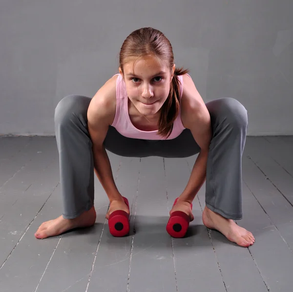 Tonåring flicka göra övningar med hantlar att utveckla med hantlar muskler på grå bakgrund. Full längd porträtt av tonåring barn tränar med vikter. — Stockfoto