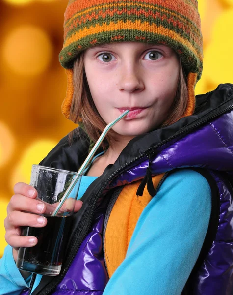 Chica con mochila y sombrero beber cola sobre fondo amarillo — Foto de Stock