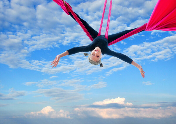 child hangs upside down on aerial silks in sky