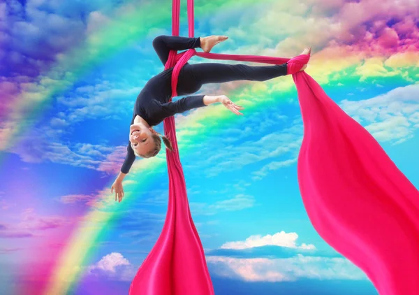 Niño cuelga boca abajo en las sedas aéreas en el cielo del arco iris —  Fotos de Stock