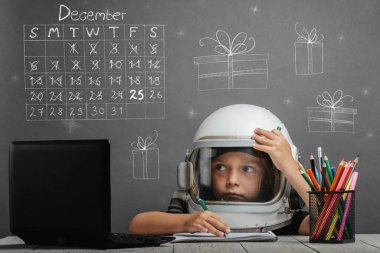 Çocuk, astronot kaskı takarak okulda uzaktan çalışıyor. Noel teması.