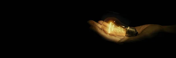 incandescent light bulb in a hand on black background