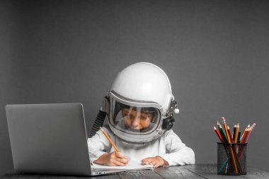 Çocuk, astronot kaskı takarak okulda uzaktan çalışıyor. Okula geri dön.