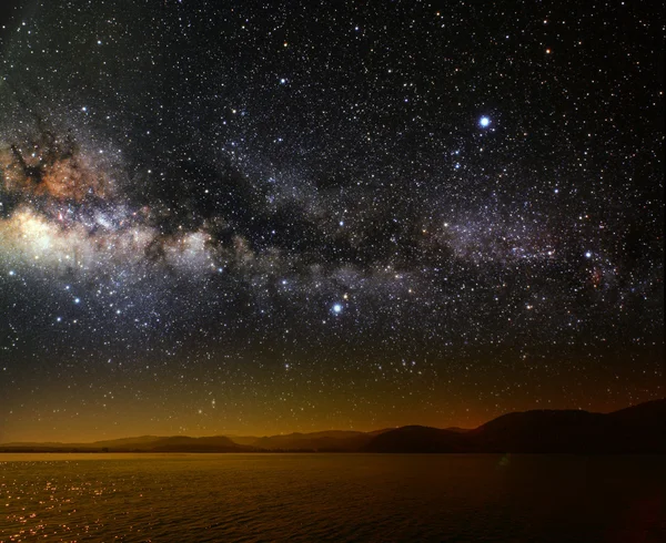 Mes sobre un cielo estrellado de fondo reflejado en el mar. — Foto de Stock