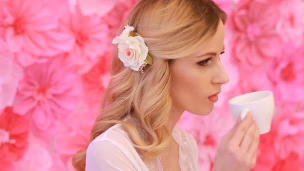 Young beautiful bride drinking from white cup on pink flowers background — Stock Video