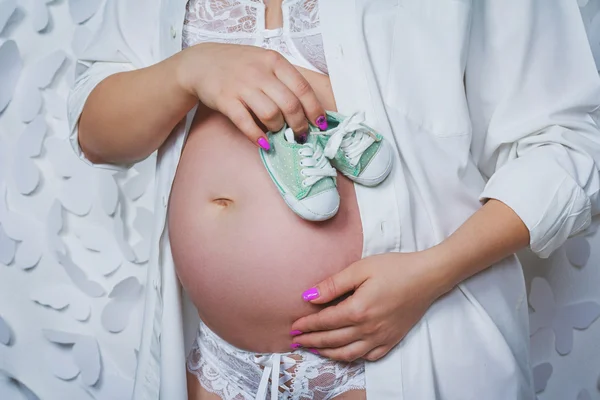 Femme enceinte tenant son ventre avec deux bottes de bébé — Photo