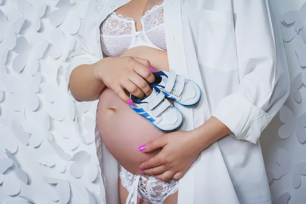 Kobieta w ciąży trzymając jej brzuch z dwóch buty dla dzieci — Zdjęcie stockowe