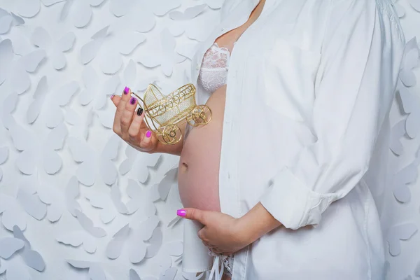 Mujer embarazada sosteniendo pequeño bebé buggy cerca de su vientre — Foto de Stock