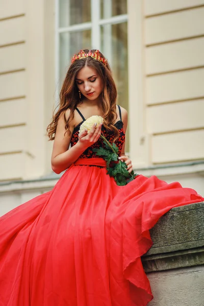 Krásná mladá žena v červených šatech drží květ — Stock fotografie