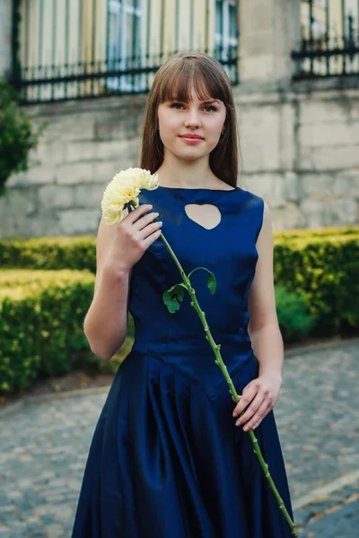 Mooie jonge vrouw in blauwe jurk houdt de bloem — Stockfoto