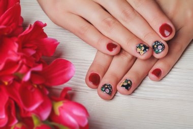 Red nail art with printed flowers on wooden background