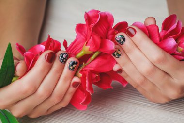 Red nail art with printed flowers on wooden background