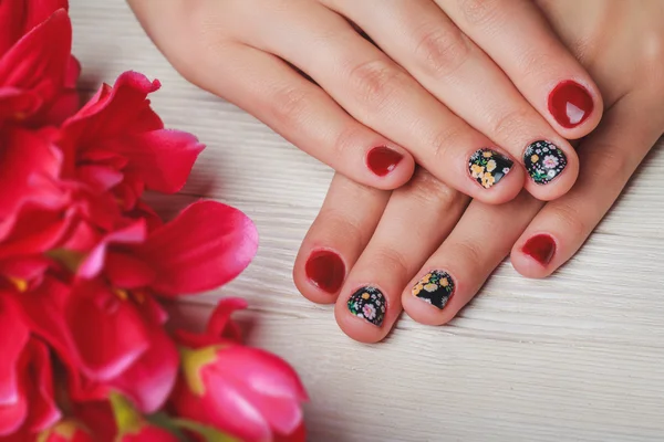 Red nail art with printed flowers on wooden background Stock Photo