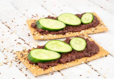 Gri ahşap arka planda zeytin ezmeli sandviçler ve salatalık..