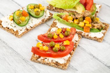 Kraker, peynir, ton balığı ve sebzeli sandviçler gri ahşap arka planda..