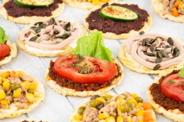 Zeytinli ve kurutulmuş domates ezmeli kinoa krakerleri, gri ahşap arka planda ton balığı ve sebze..