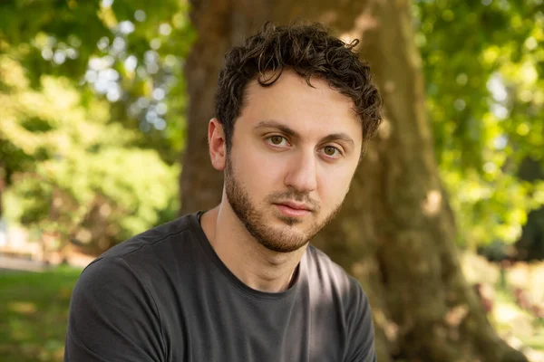 Handsome Bearded Man Curly Stylish Hair Gray Shirt Sitting Outdoors — Stock Photo, Image