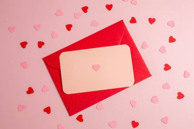 Kağıt kartlı kırmızı zarf ve pembe arka planda küçük pembe ve kırmızı kalpler..