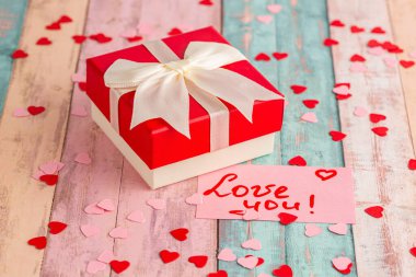Yay ile hediye kutusu, metin ile kağıt kart Seni seviyorum, küçük kırmızı ve pembe kalpler renkli ahşap arka plan.