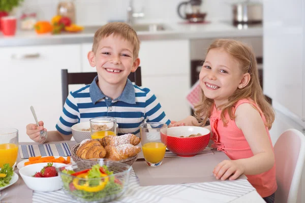 Två glada barn äter frukost i köket — Stockfoto