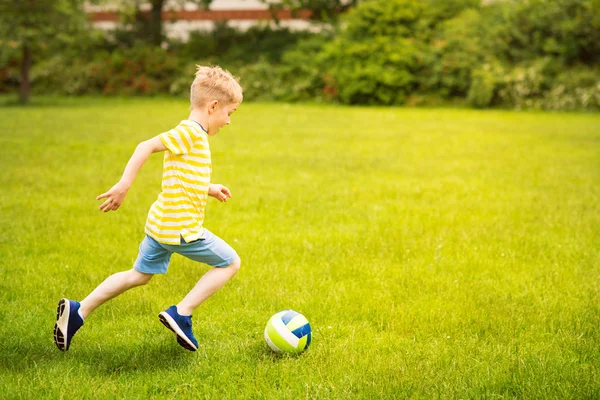 Sportivo ragazzo gioca a calcio nel parco soleggiato — Foto Stock