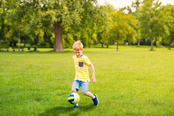Sportivo ragazzo gioca a calcio nel parco soleggiato — Foto Stock