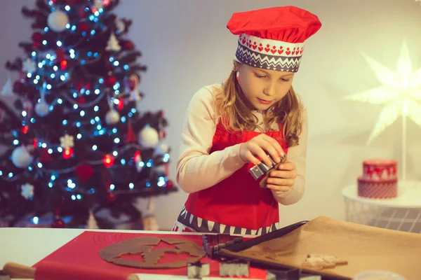 漂亮的小女孩在家里用背景上的圣诞树装饰各种形式的圣诞饼干 — 图库照片