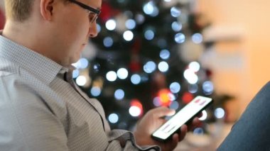 Genç adam akıllı telefonuyla internetten alışveriş yapıyor ve almak için Noel hediyesi arıyor.