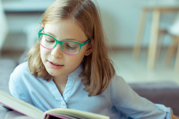 Happy pretty teen girl reading book at desk at home during pandemic distance learning 