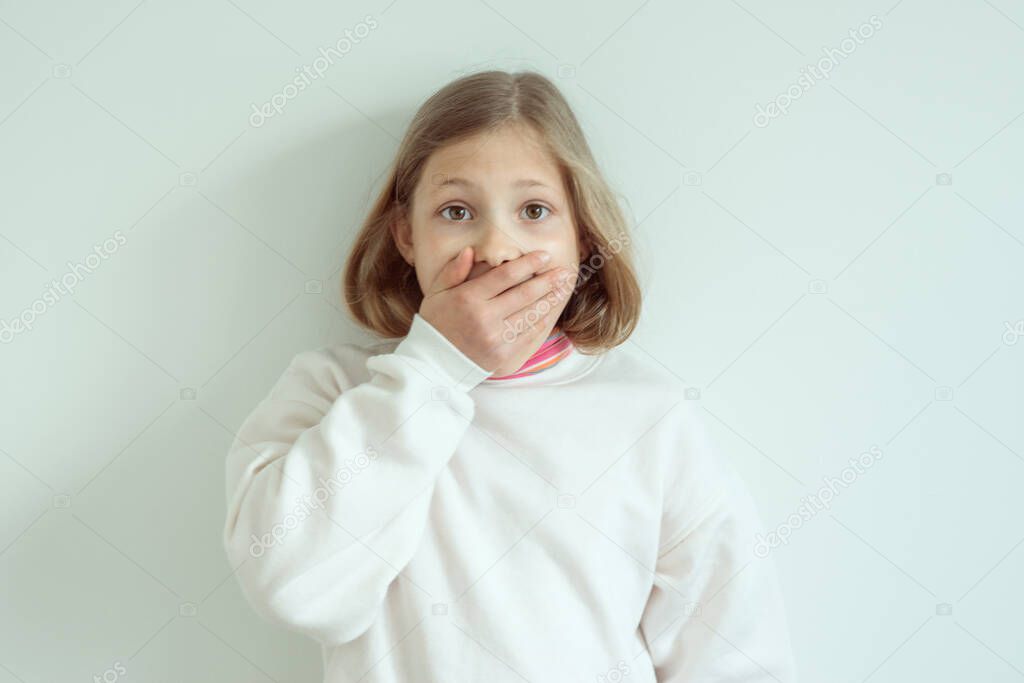 Amazed funny little girl with widely opend eyes shut her mouth with hand